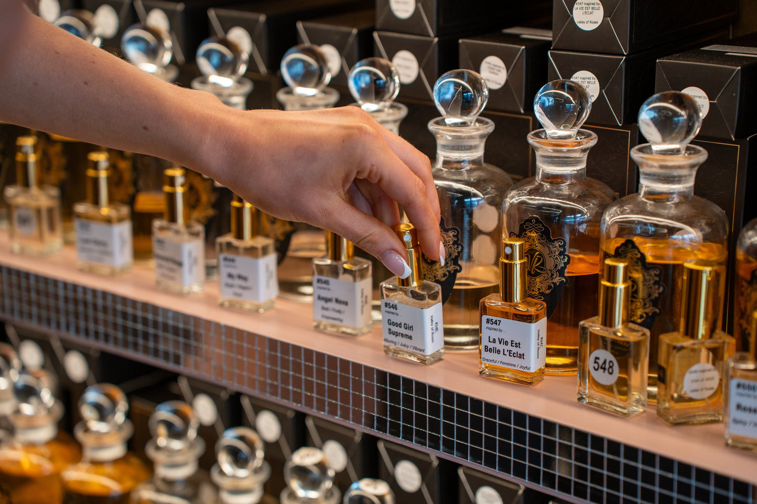 Hand choosing a travel size perfume from a shelf, ideal as stocking fillers for her: travel size perfumes, hand cream gift set picks, and soy candles.